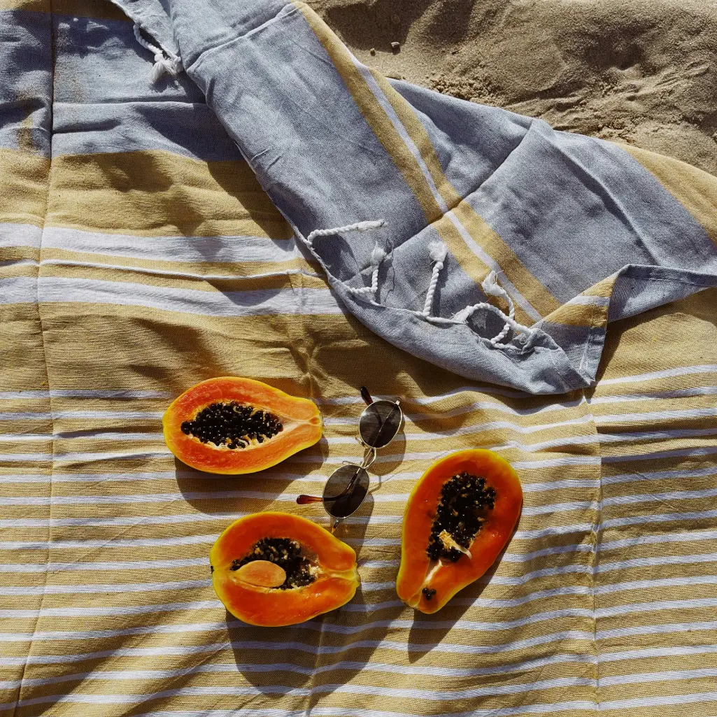 Canga de praia com mamão e óculos de sol na areia